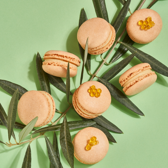 Mehrere Macarons naturfarben auf einem grünen Hintergrund, dekoriert mit gelbem Gelee.