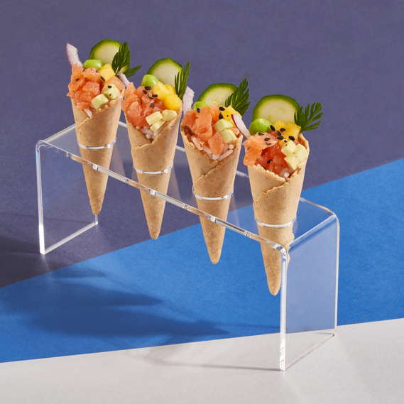 Vier kleine Waffelhörnchen mit buntem Fischtartar und Gemüse dekoriert.